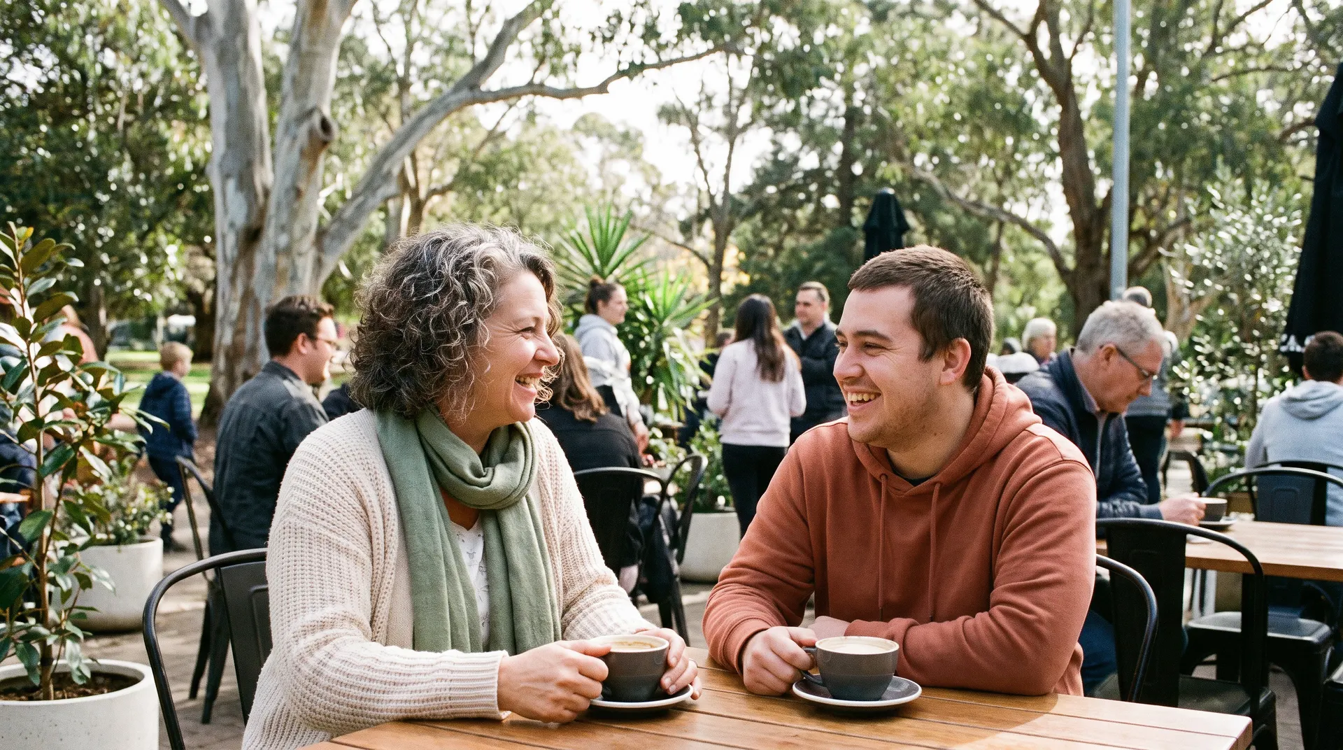 A woman and a young man laughing over coffee at an outdoor cafe