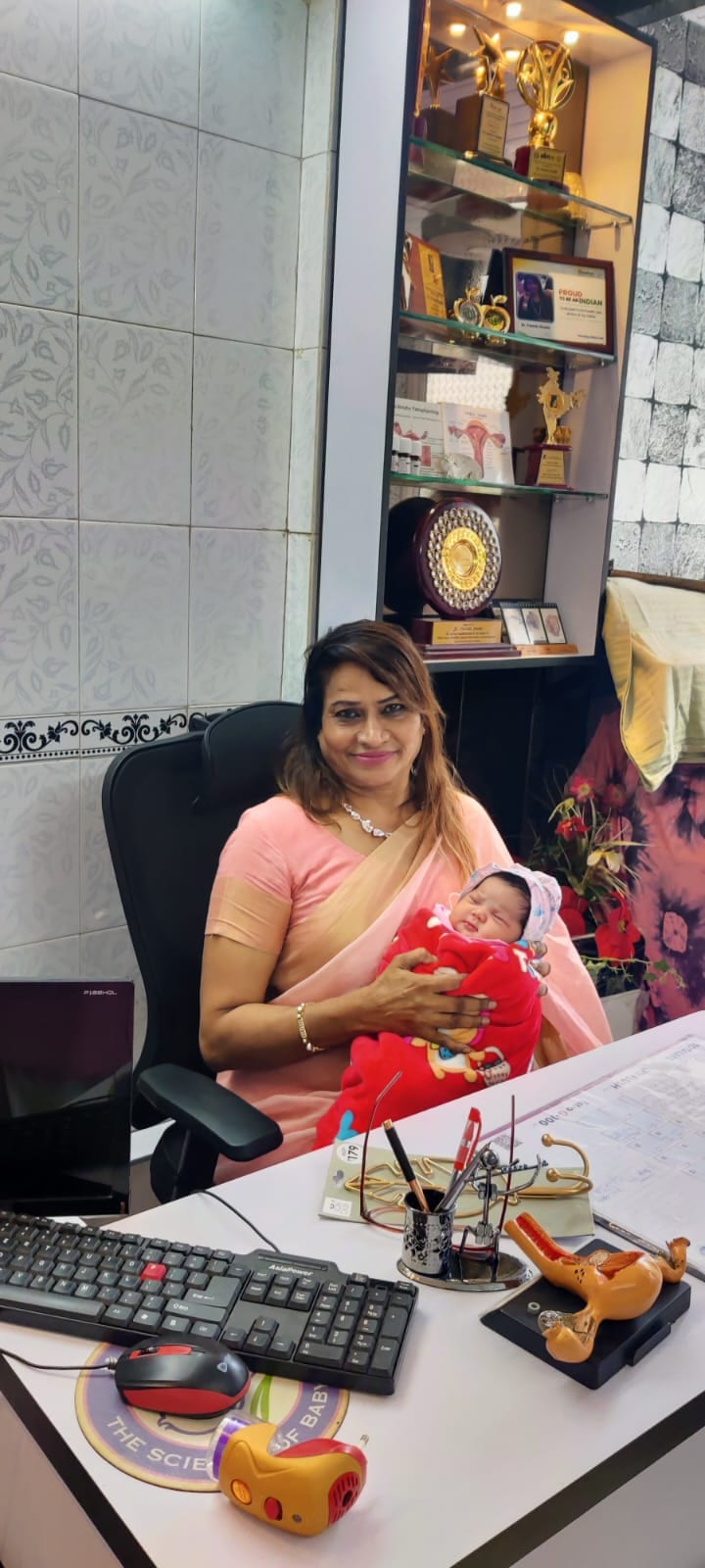 Dr. Fehmida Shaikh holding a newborn baby beside clinical recognition awards